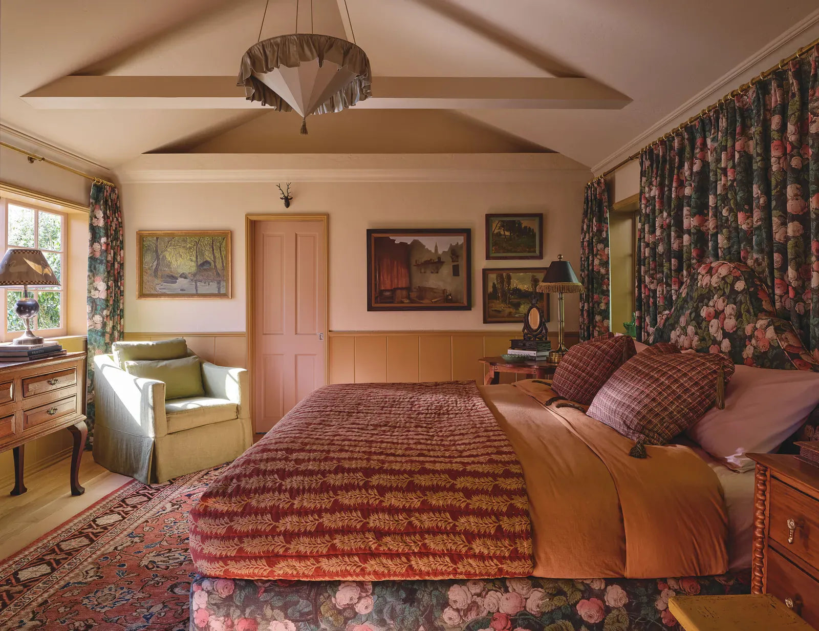 John Derian’s Rose Mosaic Forest fabric—used on the bed and for the curtains—defines the primary bedroom. Samarcande pendant light from Ebur; vintage artwork; antique Persian rug. Nightstand use Modern Matter hardware from the Pierce & Ward Collection .