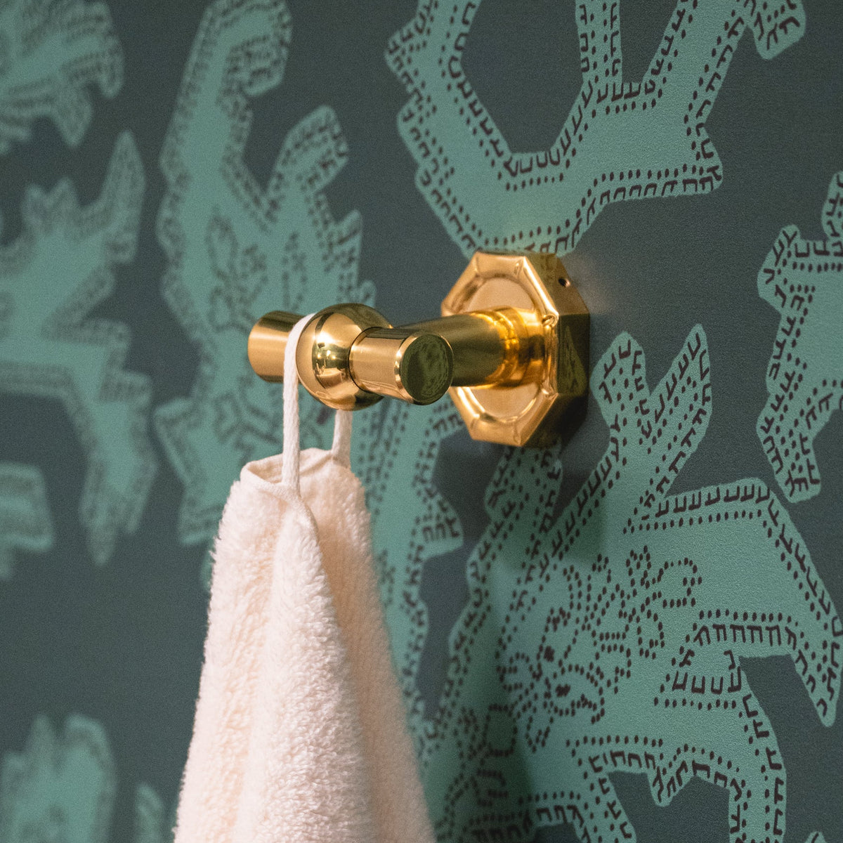 Pink towel hanging on a solid brass bath hook against a green patterned wall
