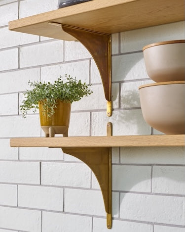Wooden shelves with decorative brackets against a white tiled wall, featuring potted plants and bowls.