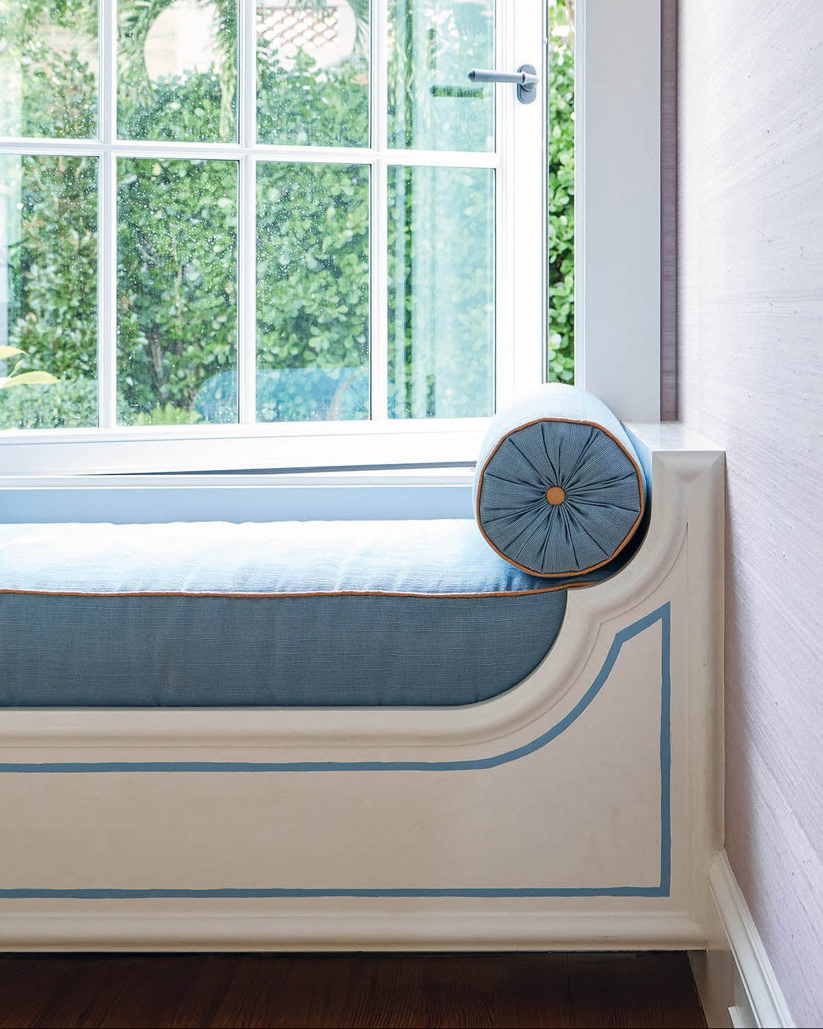 Custom window seats—trimmed with crisp Pierre Frey piping—invite lazy afternoons with a book and a breeze. The cobalt bolsters in Cowtan & Tout fabric pop against the neutral upholstery.