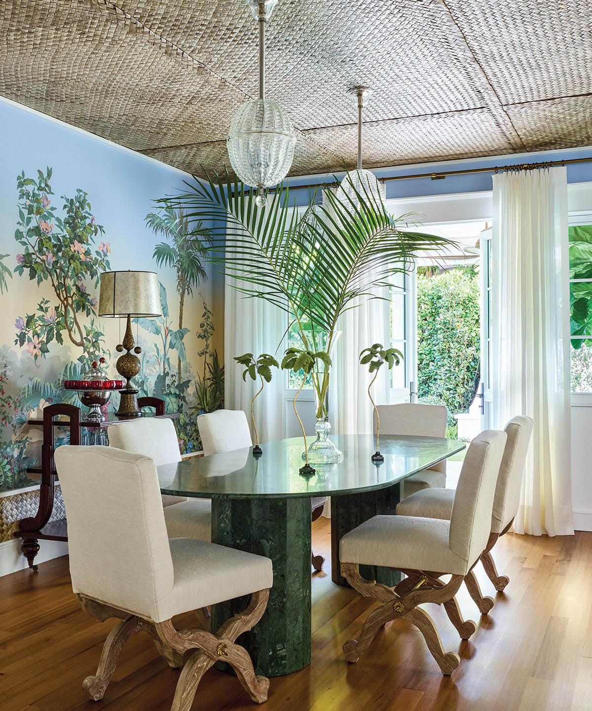 A fantastical jungle-like scene unfolds across the dining room in Zuber’s ‘Isola Bella’ wallpaper, setting the stage for a vintage green marble table and custom chairs by The Raj Company. Antique Murano pendants sparkle against a ceiling of cabana matting. “It's literally grass matting they staple down on tiki huts!” Ellen says.