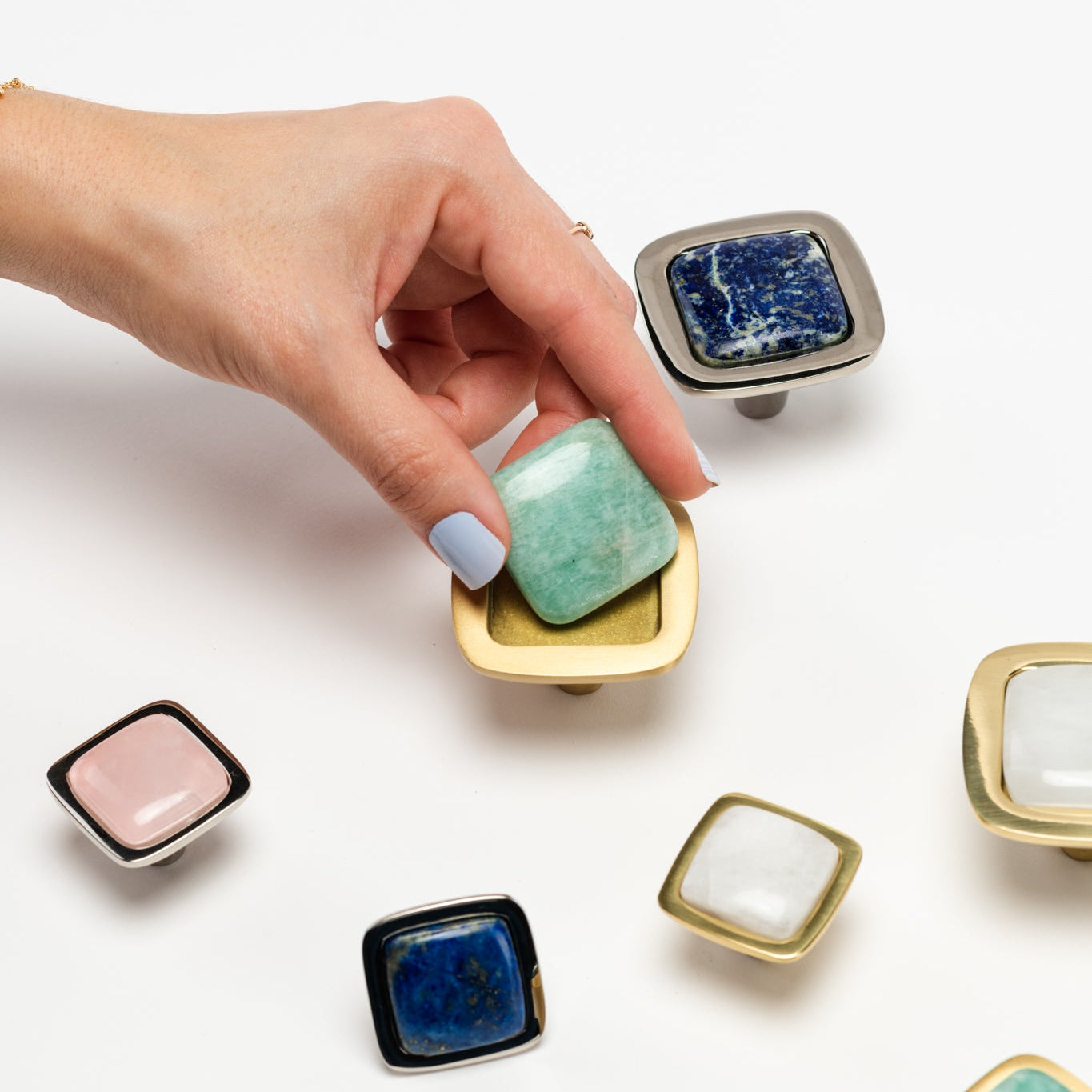 Hand holding a cabinet hardware gemstone with other similar stones on a white background