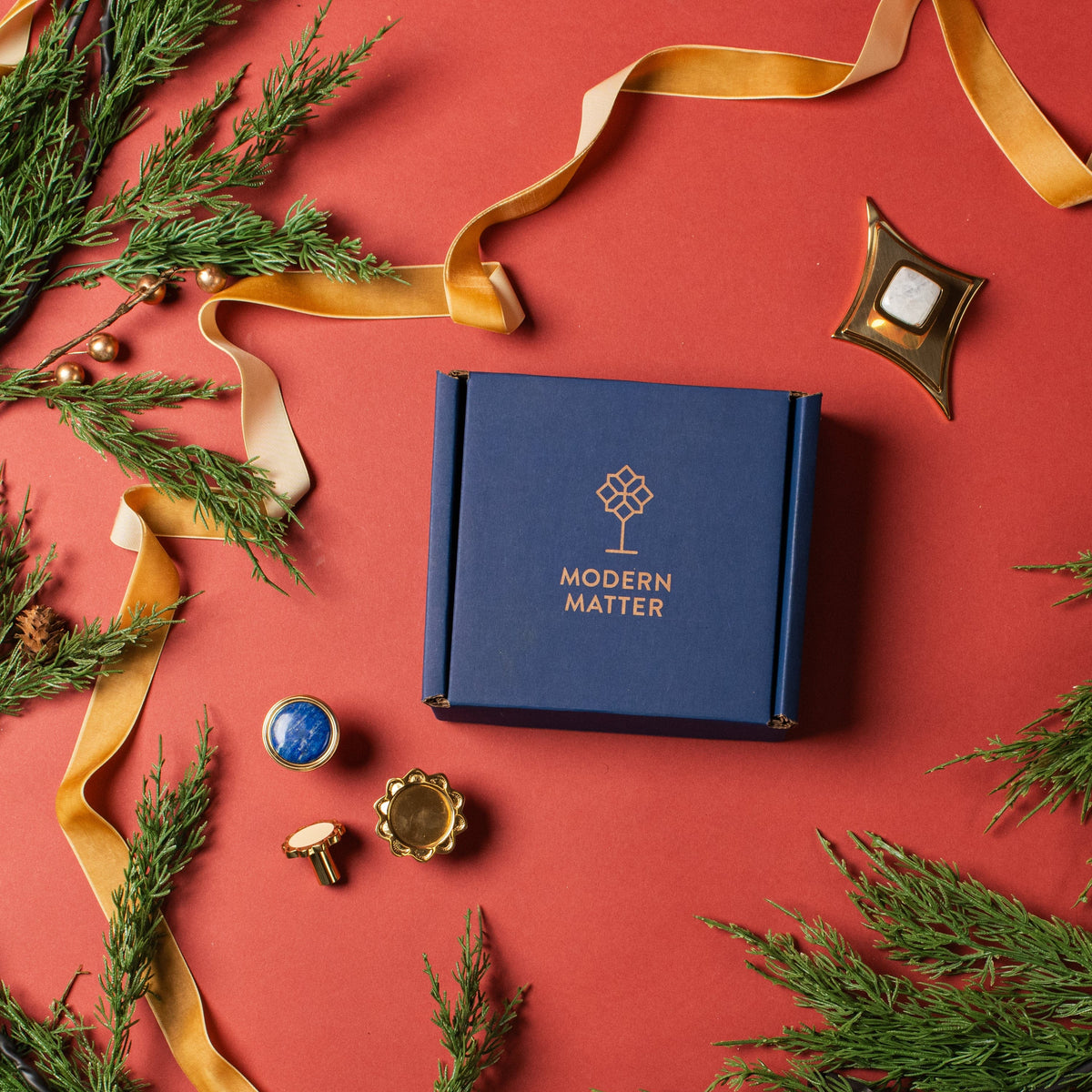 Blue box with 'Modern Matter' branding on a red background with greenery and ribbons.